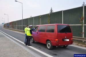 policjant i pracownik gminnej komisji wręczają ulotkę kierującemu czerwonego busa